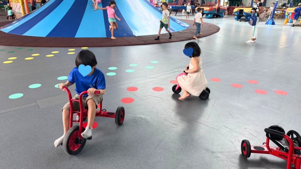 三輪車で遊ぶ子どもたち。床はカラフルな水玉模様