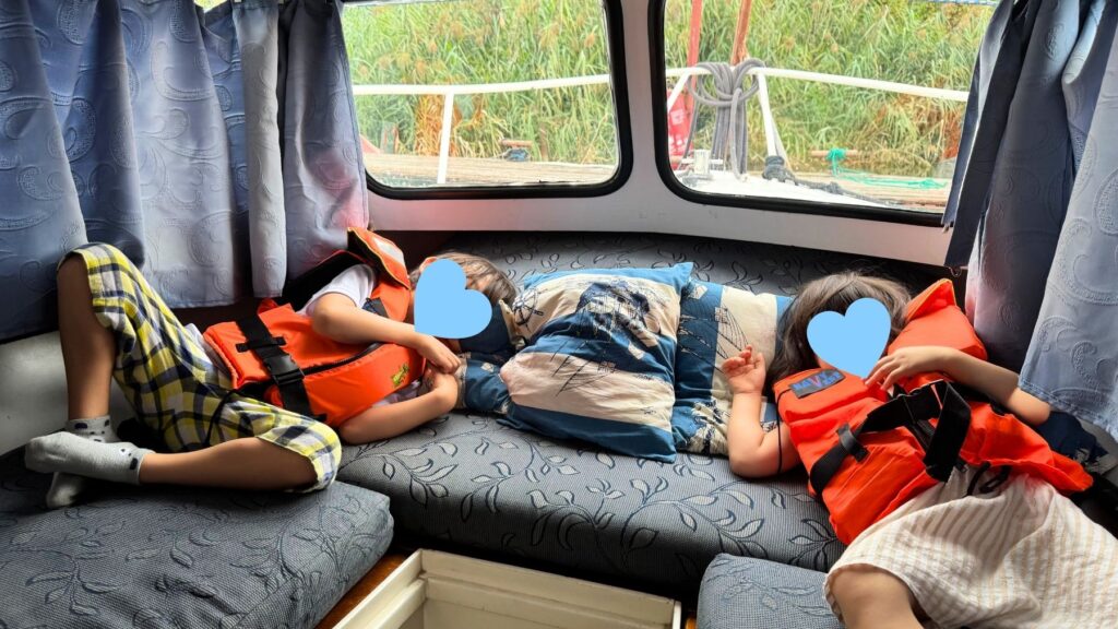 船内の寝床で横になって休む子どもたち、オレンジ色のライフジャケット姿