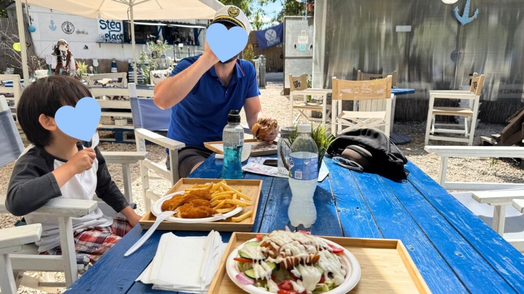 Stég Placcのテラス席で、チキンカツとポテト、サラダ、ハンバーガーを前にランチを楽しむ父と子