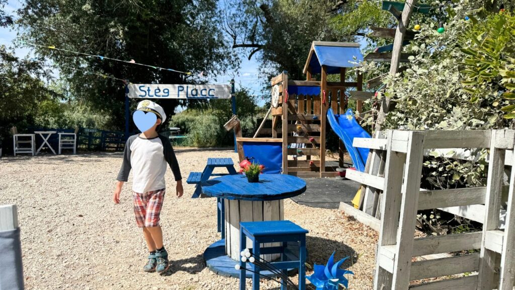 Stég Placcの看板と、滑り台やテーブルのある遊び場を歩く子ども
