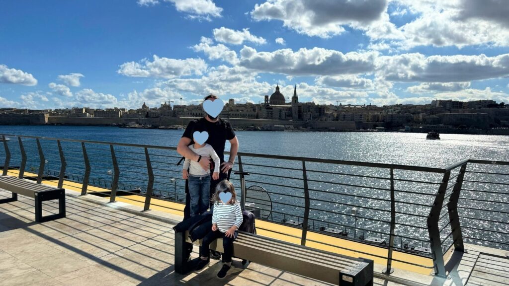 スリーマの海沿いから、海の向こうのバレッタの町並みとマウント・カーメル大聖堂のドームを背に記念撮影する家族。