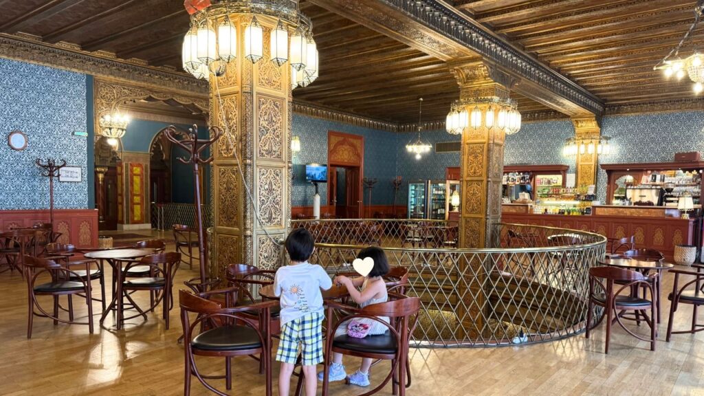 ウラーニア国立映画館のカフェに並ぶ木製のテーブルと椅子、装飾された柱と照明