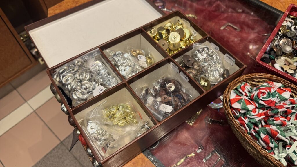 Gombudvarのカウンターに並ぶ、透明なケースに入った花形や金属風の飾りボタン